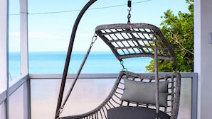 A wicker hanging chair with cushions, a metal frame, and a view of the ocean. - Luichy's Seaside Hotel (Cabo Rojo)