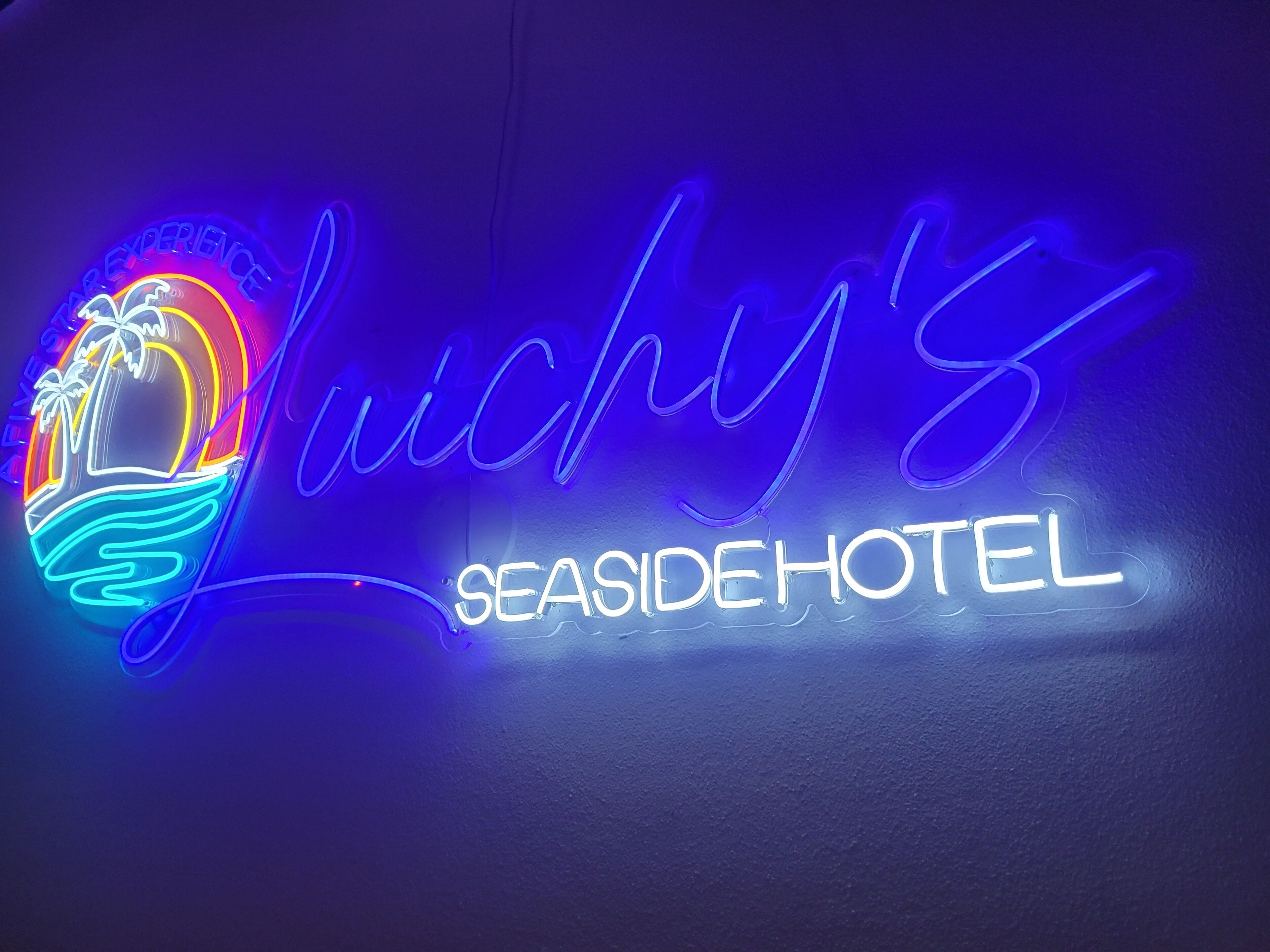 Un letrero de neón para 'Luchy's Seaside Hotel' con un diseño de playa y palmera.