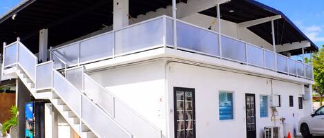Un bâtiment blanc doté d’un espace extérieur couvert, d’un escalier et d’une antenne parabolique.