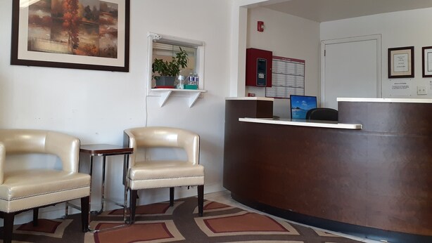 A reception area with a desk, two chairs, a potted plant, a framed picture, and a bulletin board. - Cortland Motel (Cortland)