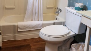 A bathroom with a bathtub, toilet, and a shower curtain. - Cortland Motel (Cortland)