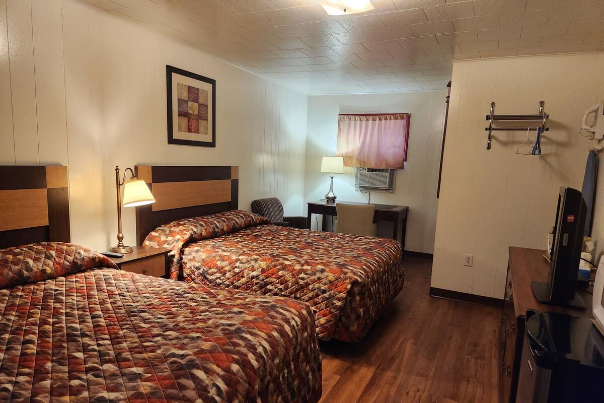 A hotel room with two beds, a desk, a chair, a TV, and a window with a curtain.