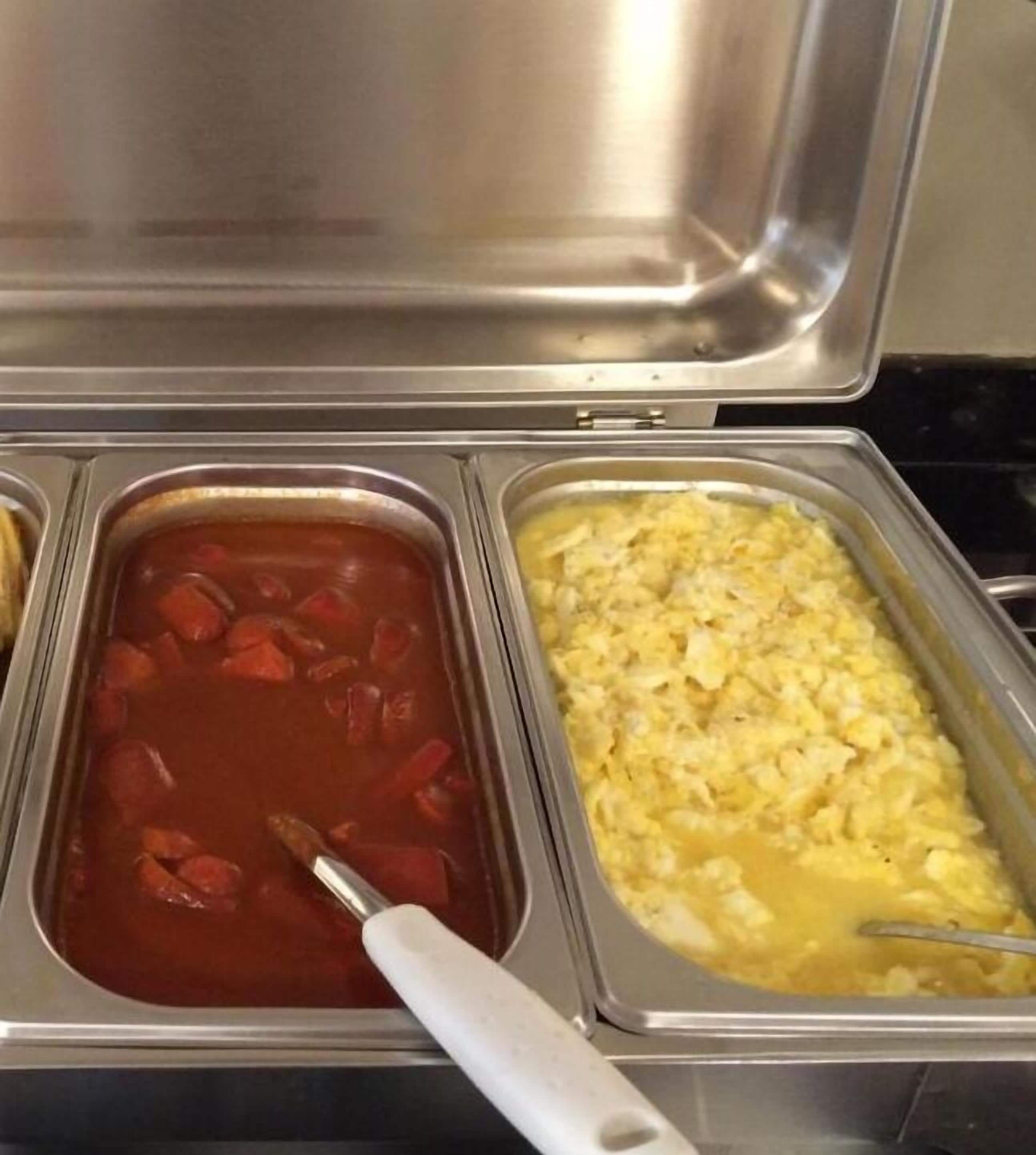 Un bufé con dos platos visibles: una sopa a base de tomate rojo y un plato de huevos revueltos amarillos.