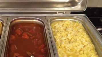 Un bufé con dos platos visibles: una sopa a base de tomate rojo y un plato de huevos revueltos amarillos.