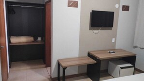 Une petite chambre d’hôtel comprenant un lit, un bureau, une chaise, une télévision, une armoire et un petit réfrigérateur.