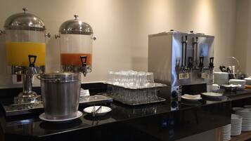Montaje de bufé con varios dispensadores de bebidas, una máquina de café y platos y vasos ordenados.