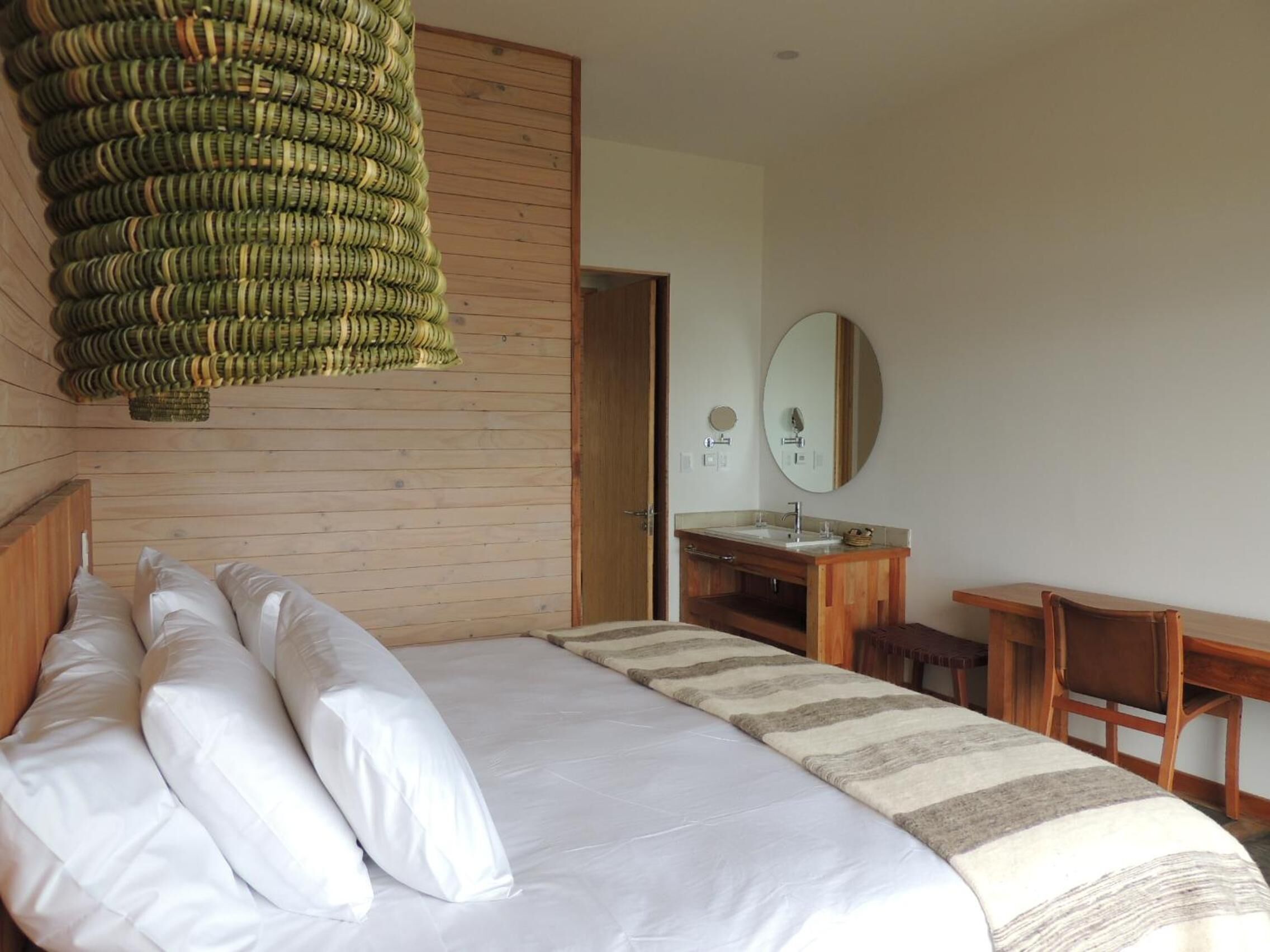 Camera da letto con un letto, cuscini, una testiera in legno, un comodino, uno specchio e una sedia a dondolo in vimini.