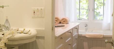 Une salle de bain avec un lavabo blanc, une baignoire, une fenêtre donnant sur des arbres et un tapis à motifs sur le sol.