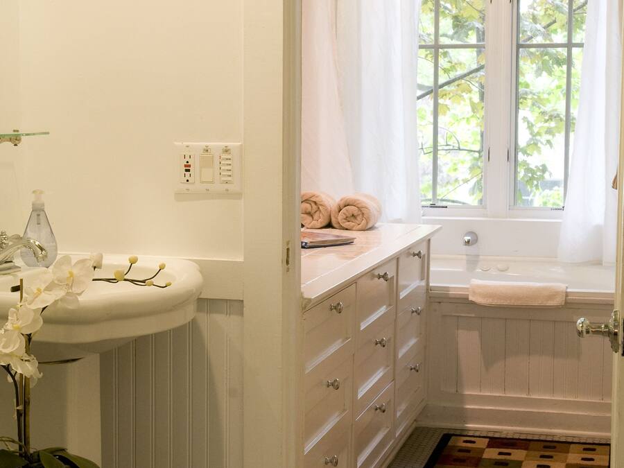 A bathroom with a white sink, a bathtub, a window with a view of trees, and a patterned rug on the floor.