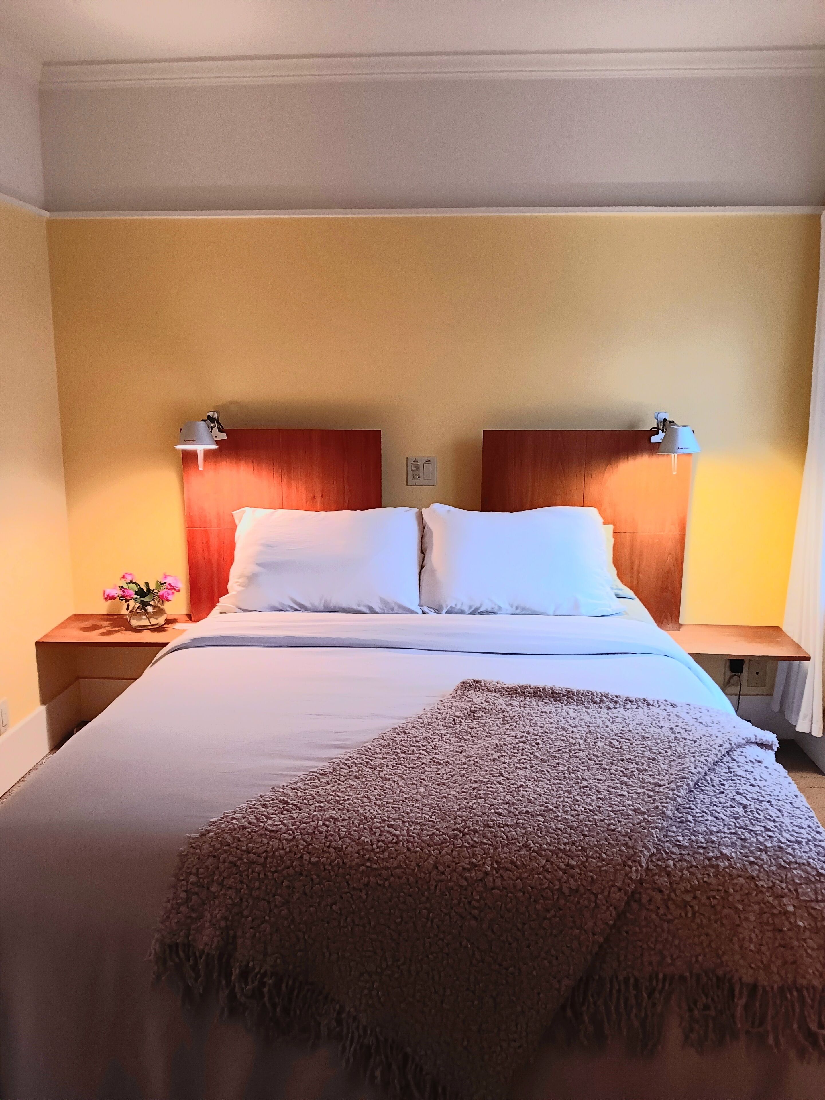 A hotel room with a large bed, wooden headboard, bedside lamps, and a nightstand with a vase of flowers.