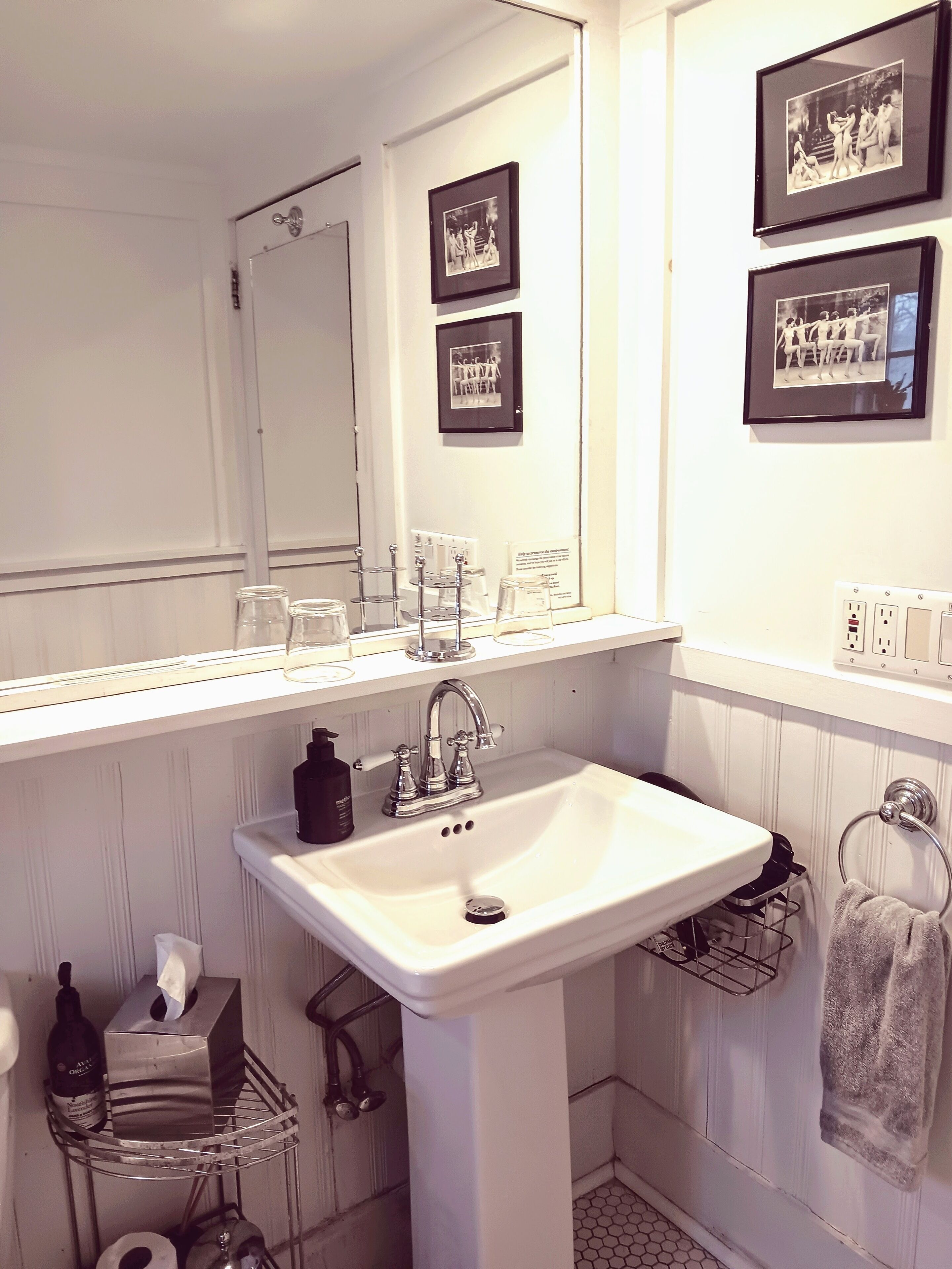 Un baño con lavamanos blanco, un espejo y fotografías en blanco y negro enmarcadas en la pared.