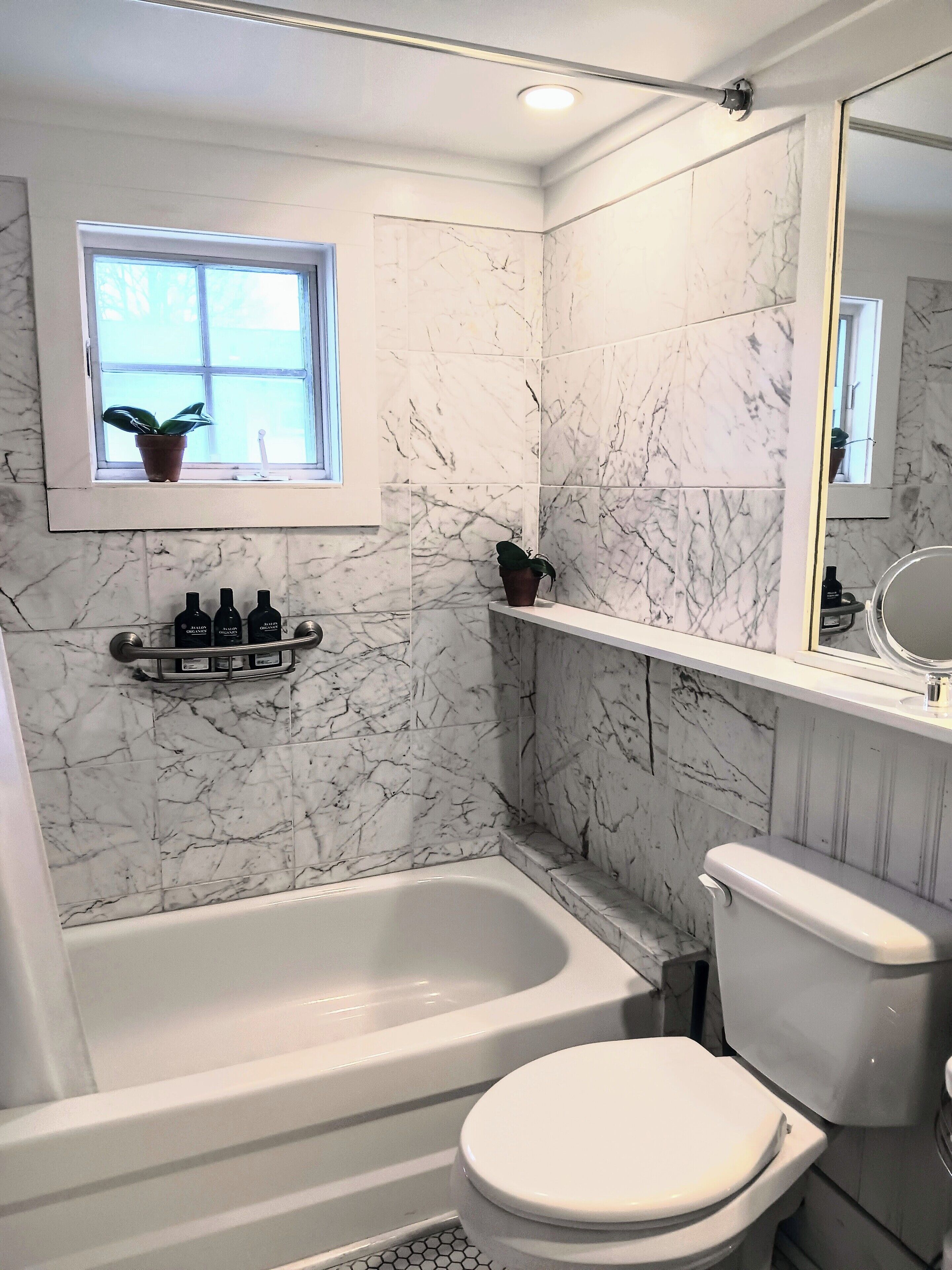 A bathroom with a bathtub, toilet, and a window with plants.