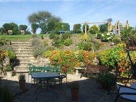 A garden patio with stone steps, green metal chairs, and a wooden bench.