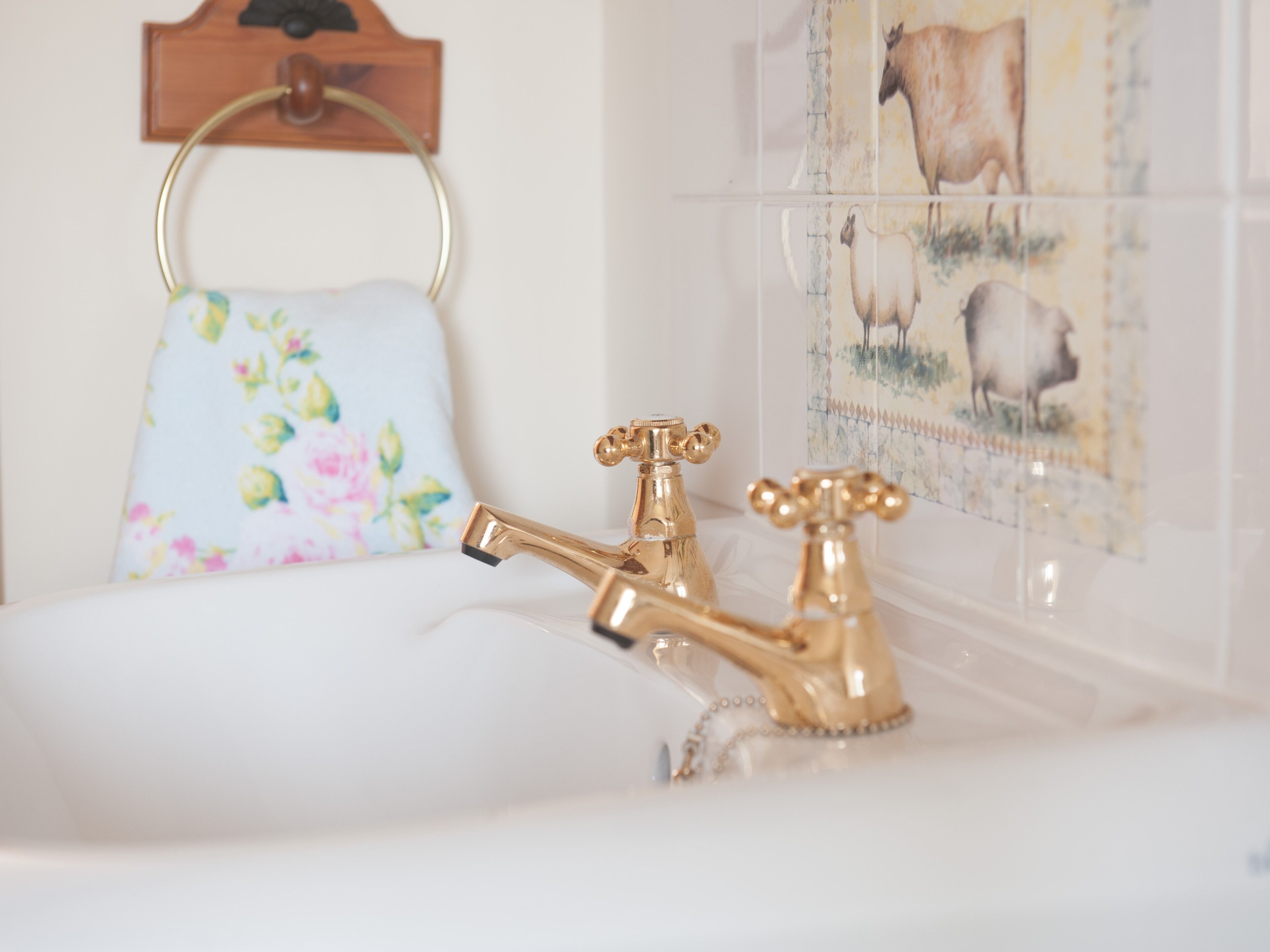 Ein Badezimmer mit goldenem Wasserhahn, einem Blumendekor-Handtuch und einer Wand mit Tierdarstellungen.