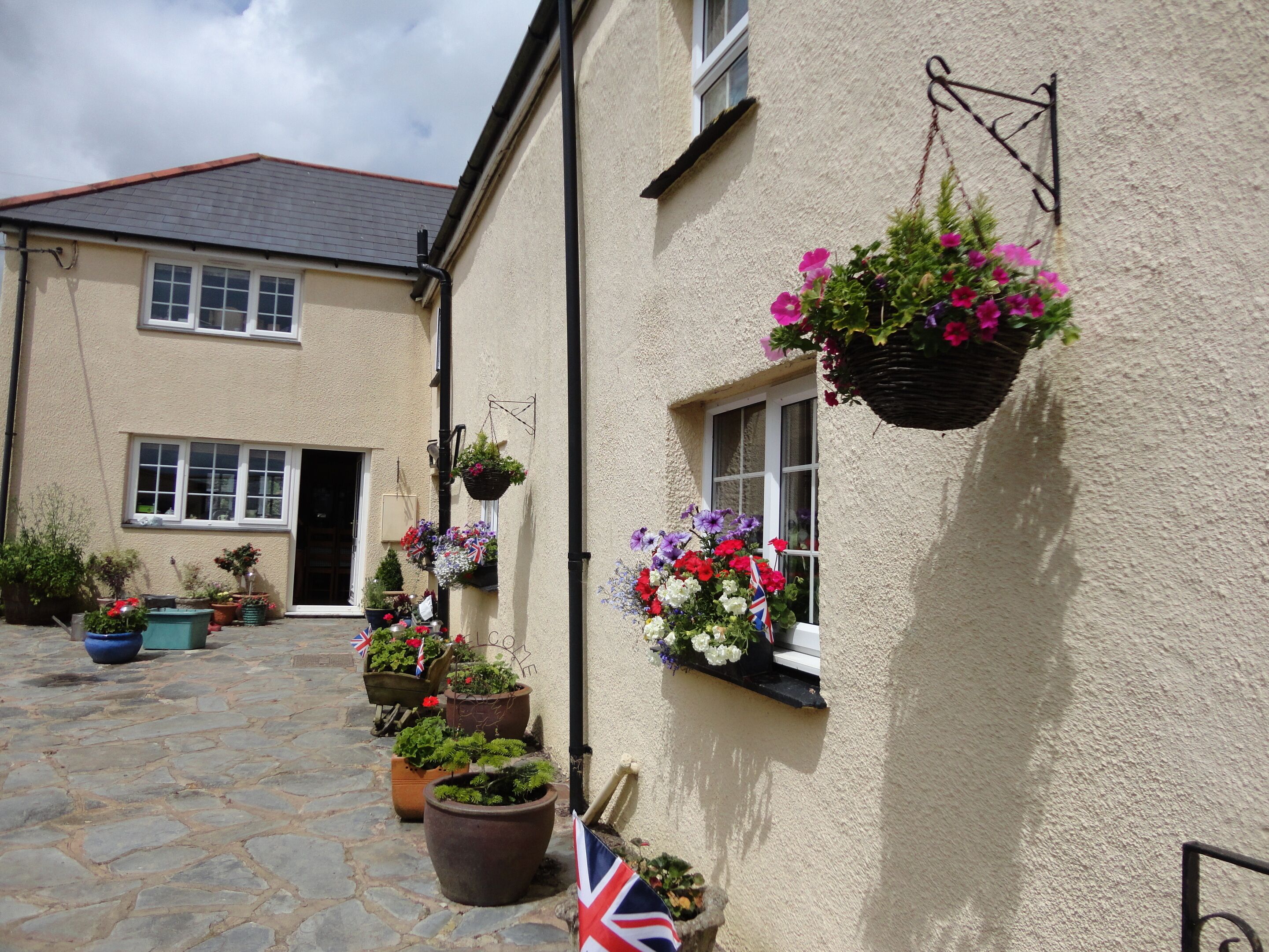 A building with multiple windows, some with hanging flower baskets, and a stone-paved courtyard.