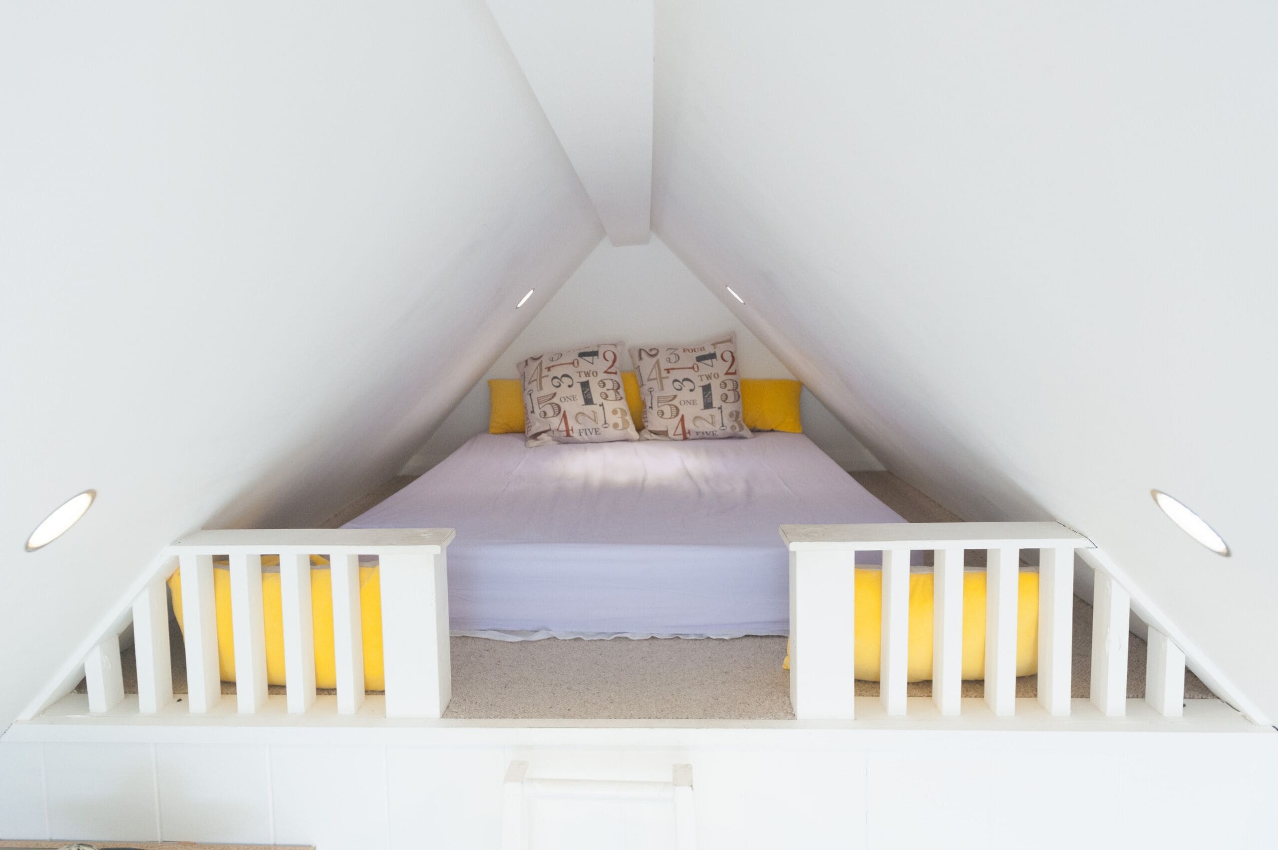 A triangular attic bedroom with a bed, pillows, and a white railing.