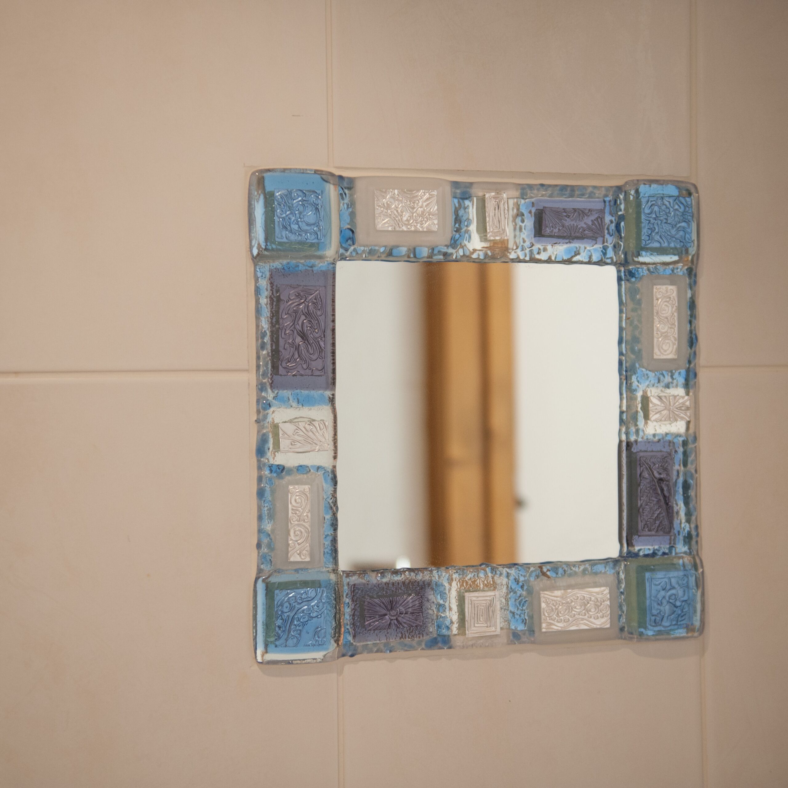 A bathroom with a square mirror framed by a mosaic tile border.