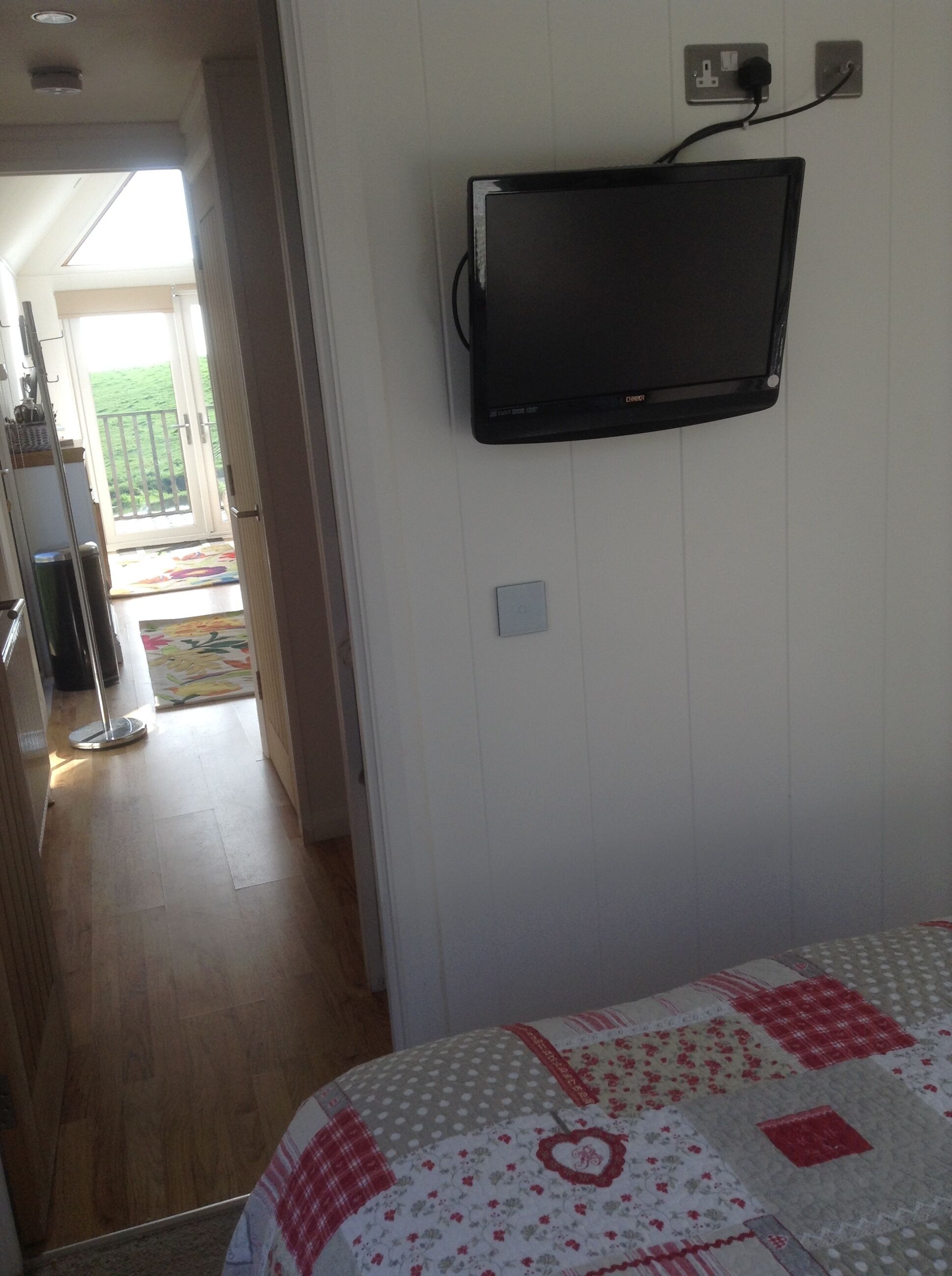 Una habitación con una cama, televisión montada en la pared y una puerta que da a un balcón.