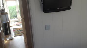 Una habitación con una cama, televisión montada en la pared y una puerta que da a un balcón.