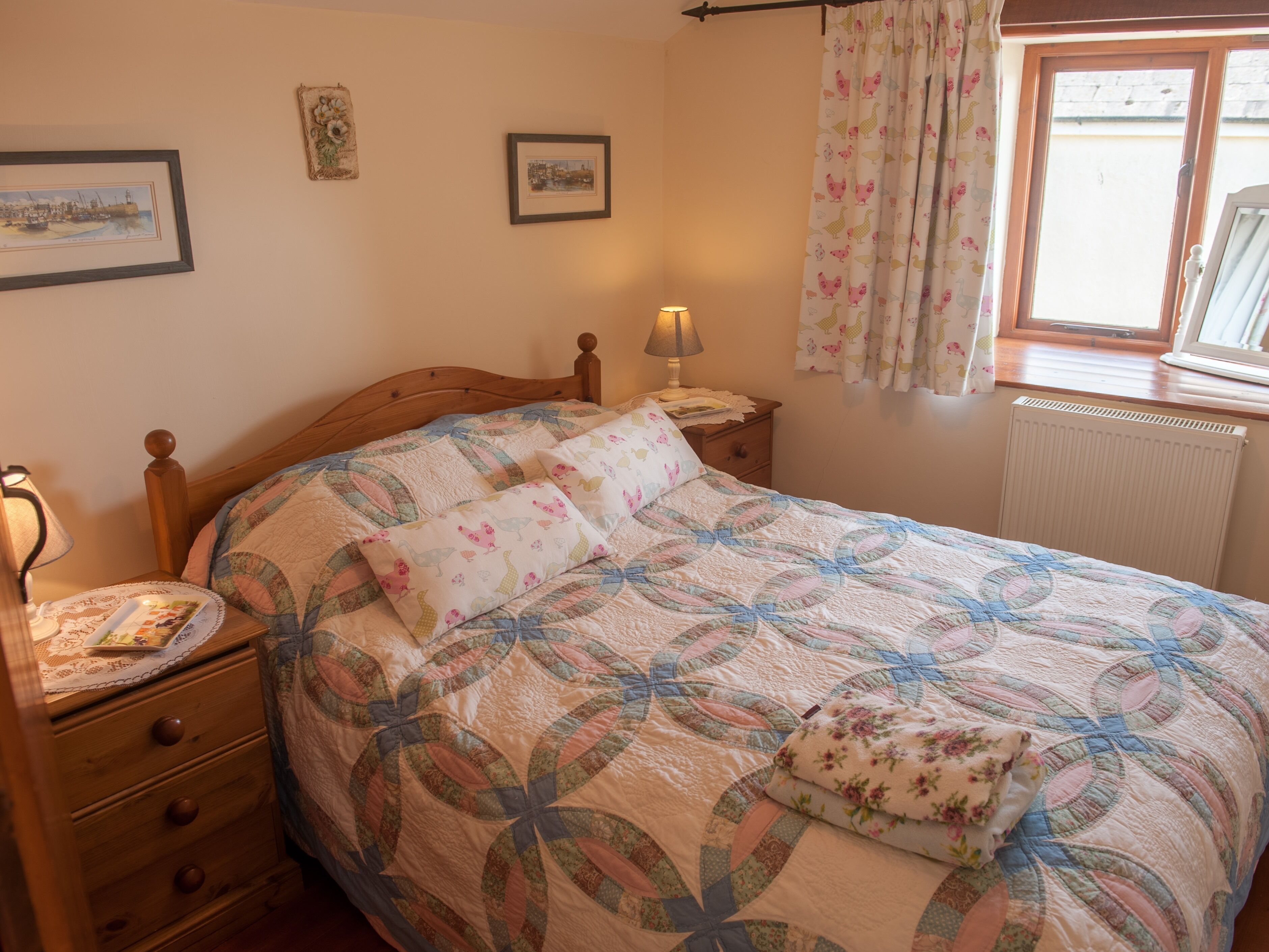 A bedroom with a wooden bed, a bedside table with a lamp, a dresser, and a window with curtains.