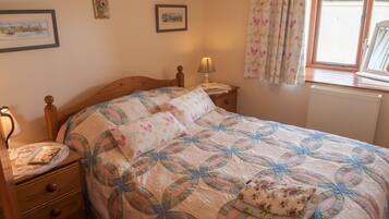 A bedroom with a wooden bed, a bedside table with a lamp, a dresser, and a window with curtains.