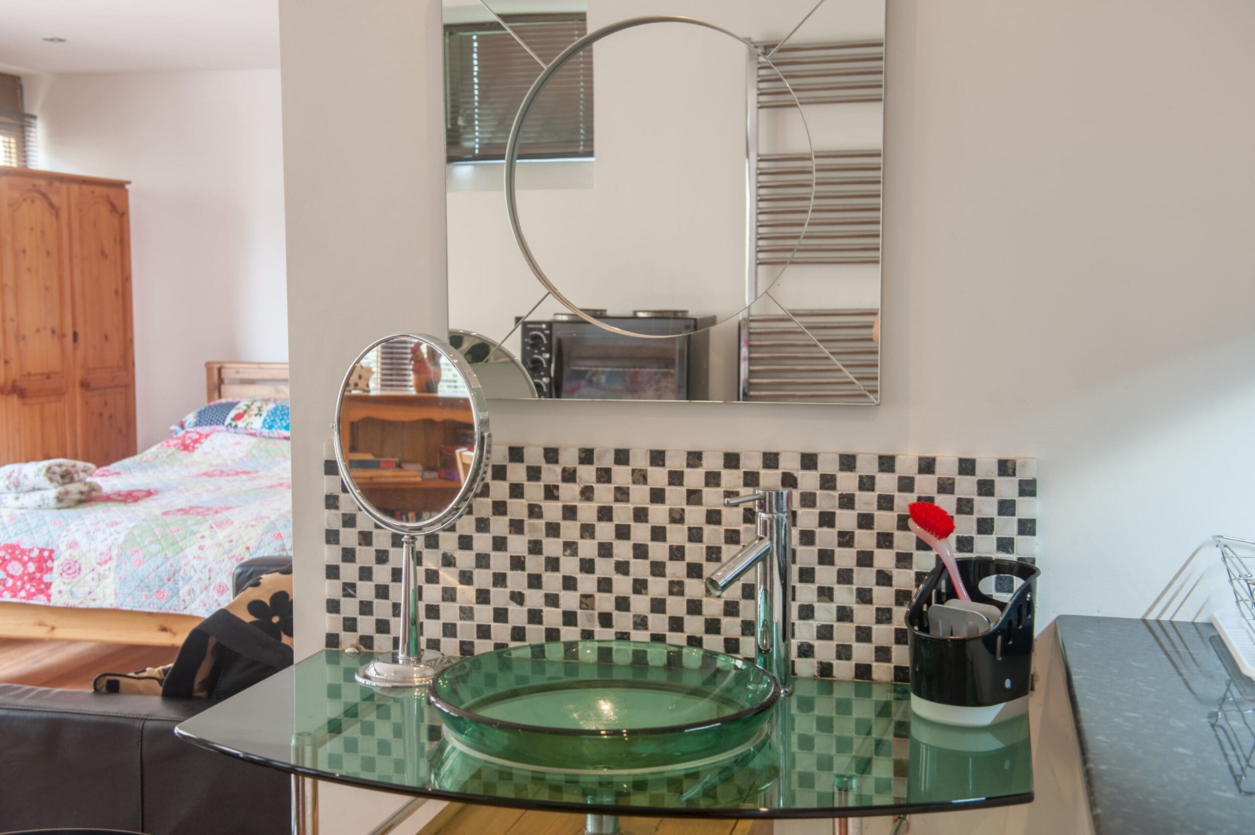 A bathroom with a glass sink, a mirror, a toothbrush holder, and a checkered backsplash.