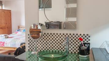 A bathroom with a glass sink, a mirror, a toothbrush holder, and a checkered backsplash.