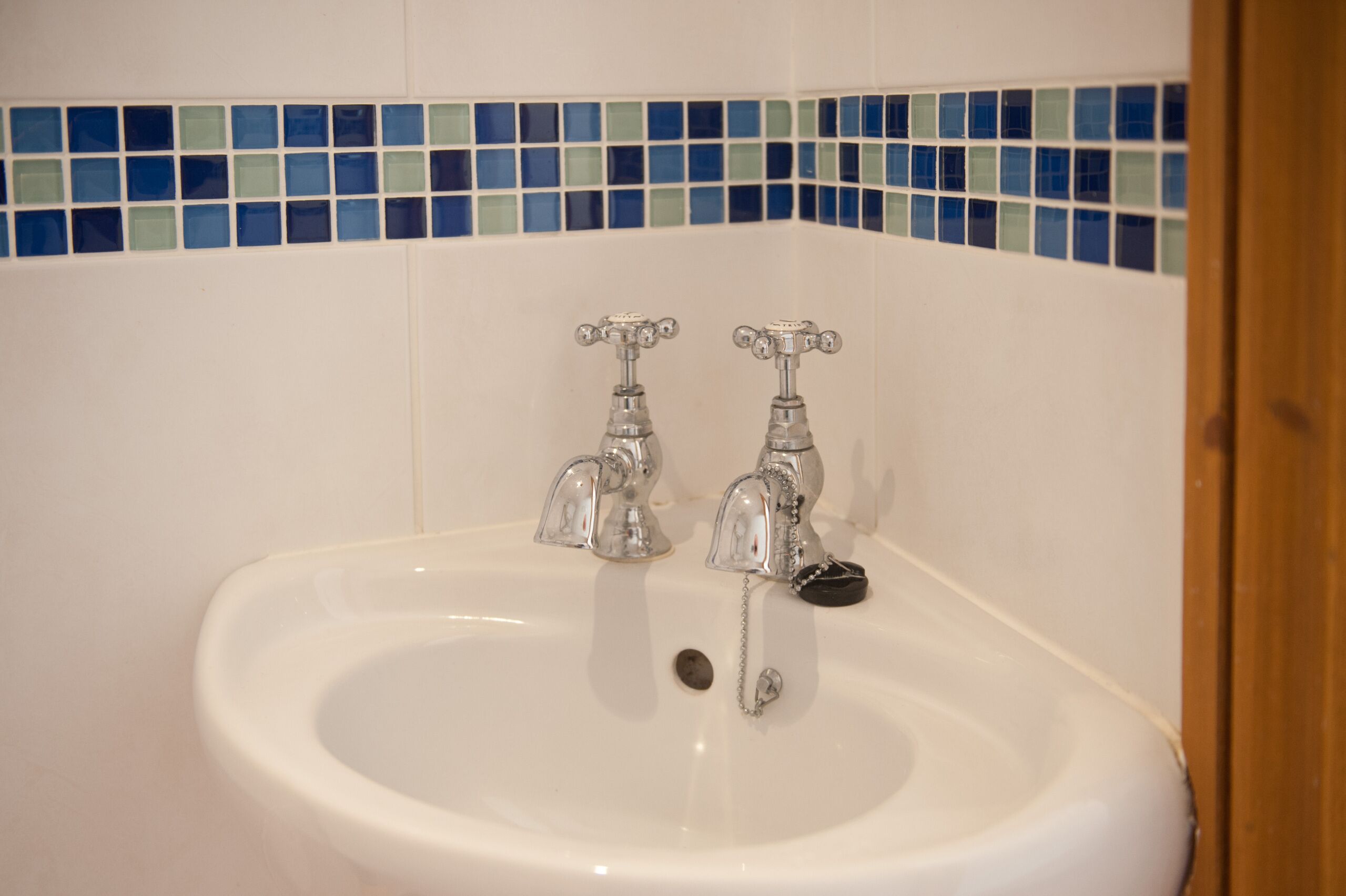 Un lavamanos con dos grifos y un borde de mosaico azul.