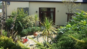 A house with a sloped roof, a front door, and a garden with various plants and a large pot.