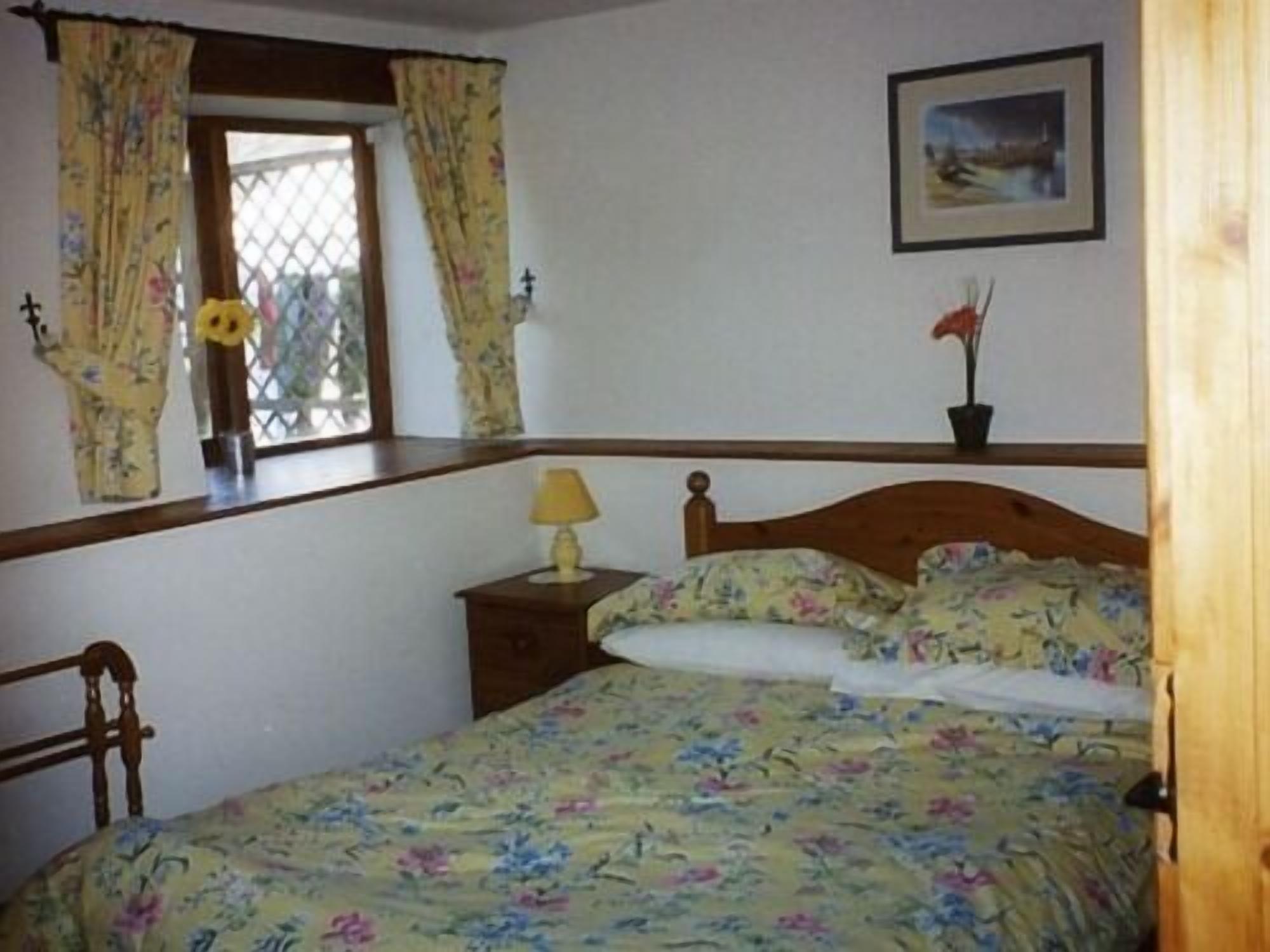 Een slaapkamer met een bed, nachtkastje, raam met gordijnen en een ingelijste foto aan de muur.