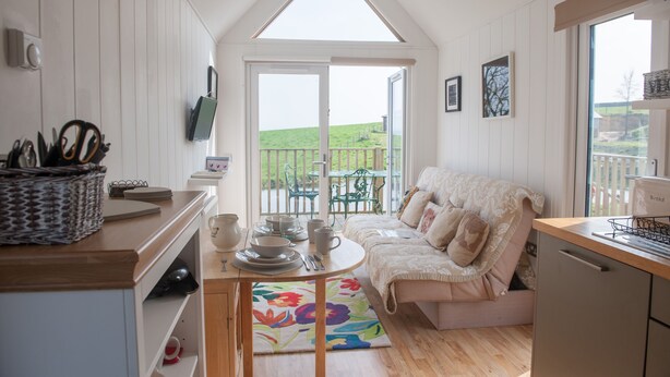 A cozy kitchen with a dining area, a sofa, and a view of a green landscape through a large window.