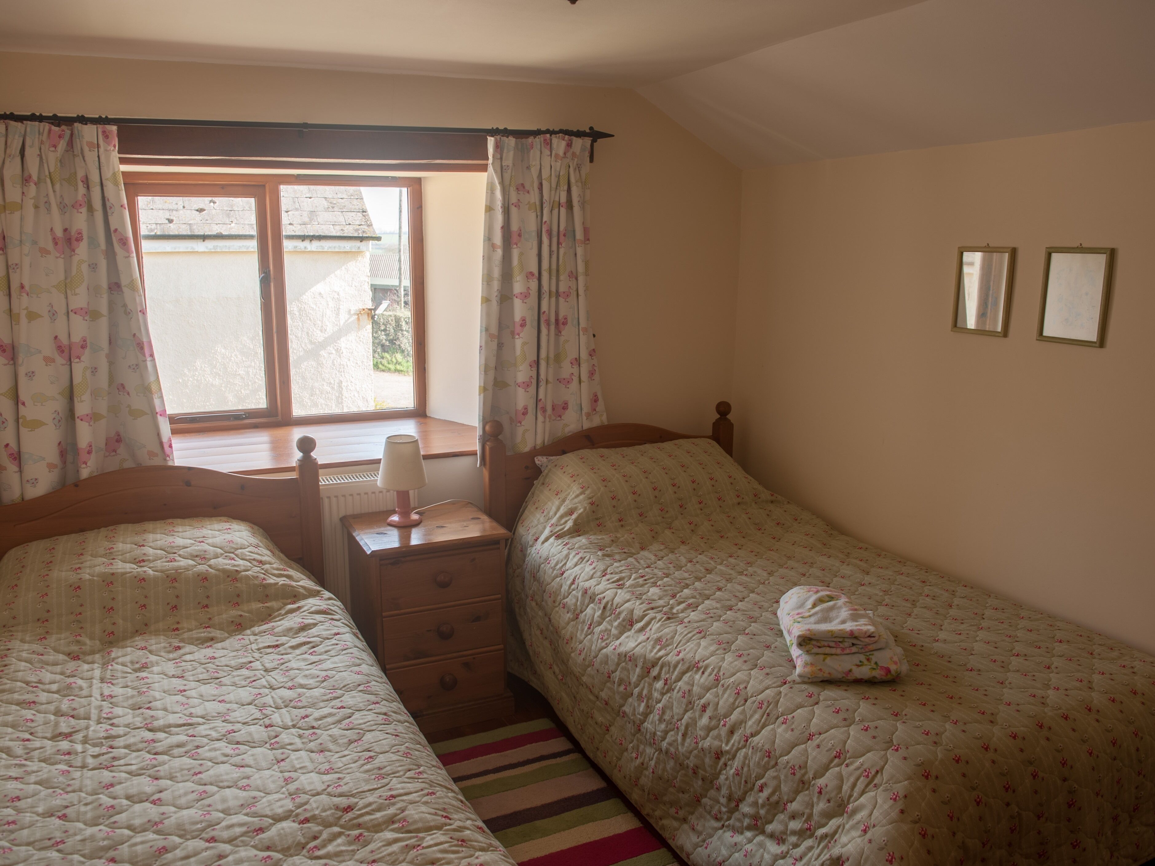 Een slaapkamer met twee bedden, een dressoir, een lamp en een raam met gordijnen.