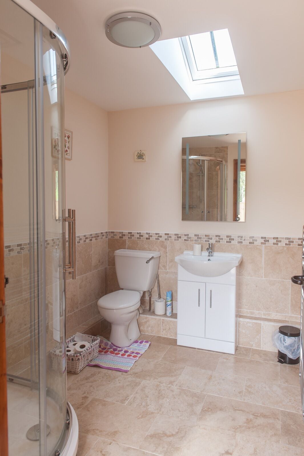 A bathroom with a skylight, a glass shower enclosure, a toilet, a sink, and a tiled floor.