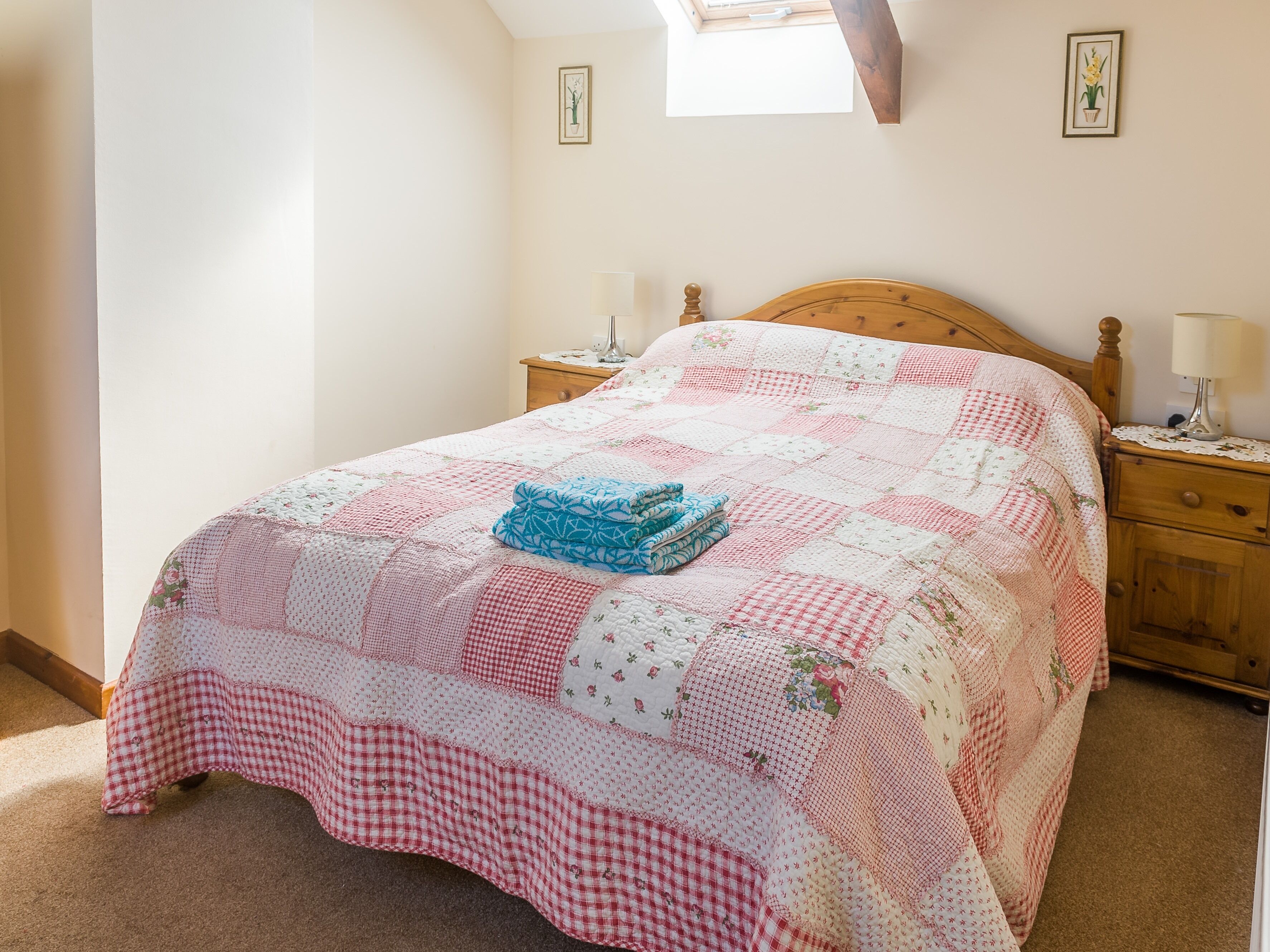 Ein Schlafzimmer mit einem großen Bett, das mit einer Patchworkdecke bezogen ist, Holz-Nachttischen mit Lampen und einem Oberlicht über dem Bett.