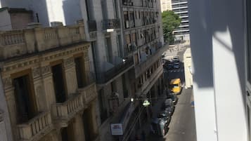 A multi-story building with balconies, a street with parked cars, and a clear sky.