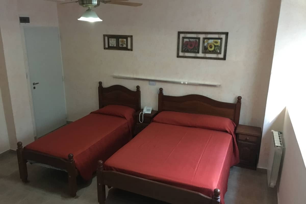 A room with two wooden beds, a ceiling fan, a white door, and two framed pictures on the wall.