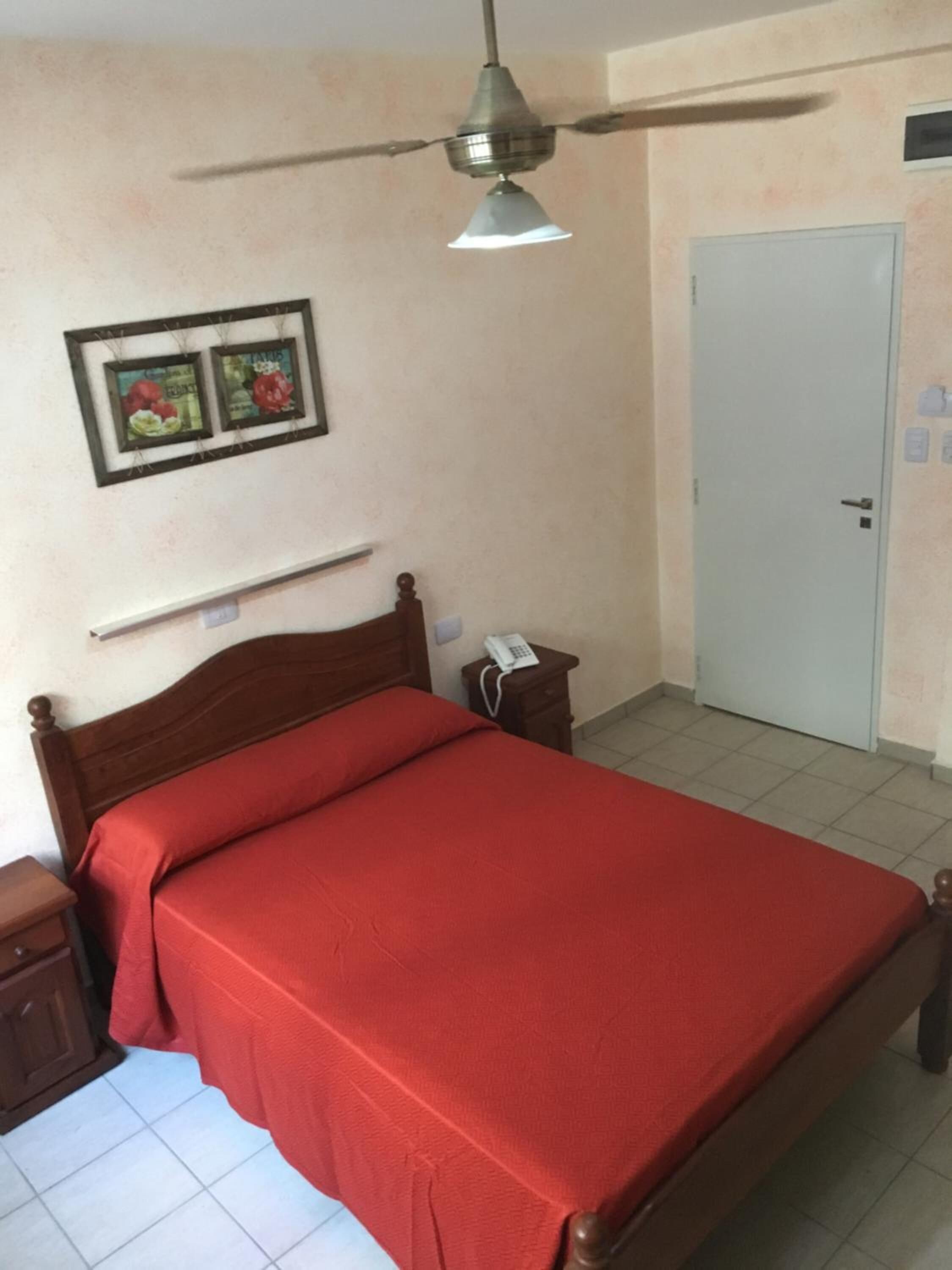 A single-bed room with a wooden headboard, a ceiling fan, a bedside table with a phone, and a door with a lock.