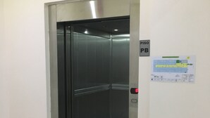 Un ascensor con interior metálico, un panel de control con un botón rojo y un cartel con el plano de los pisos en la pared.