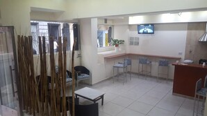 Vestíbulo de hotel con mostrador de recepción, varias sillas, un televisor montado en la pared y un ventanal con vistas al exterior.