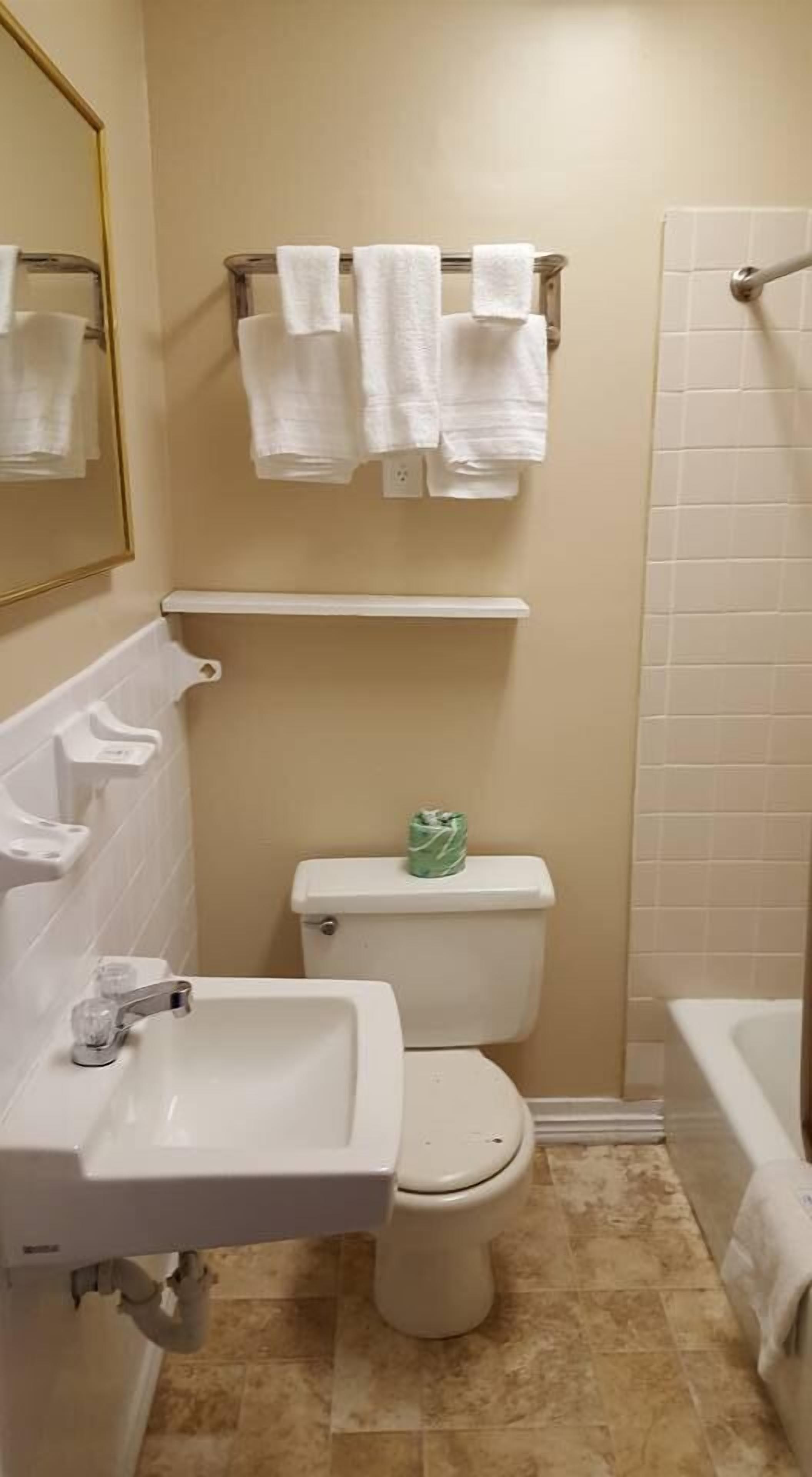 Un baño con lavamanos, inodoro y bañera. Hay toallas colgadas en un tendedero sobre el inodoro.