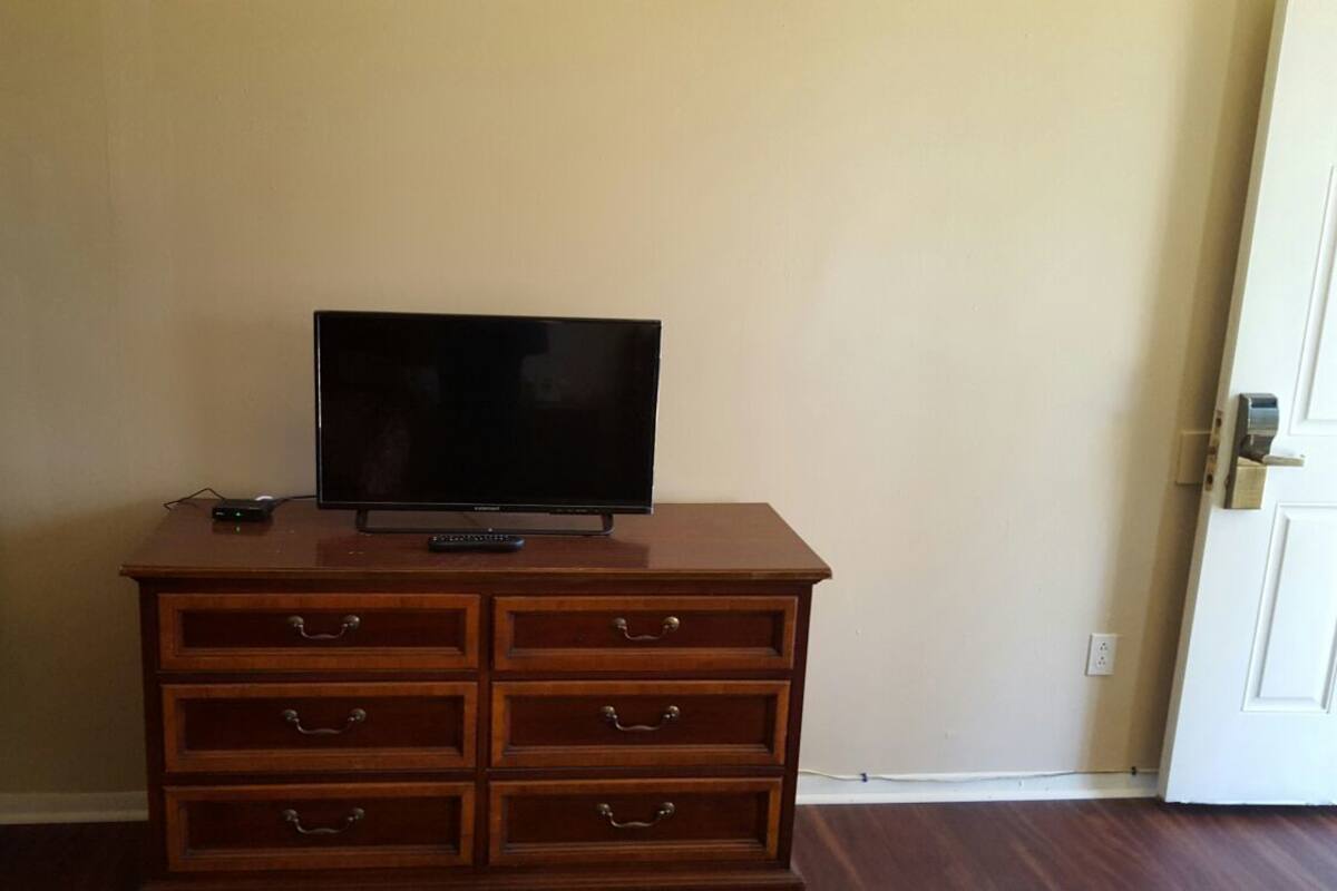 A room with a wooden dresser, a television on top, and a door to the right.