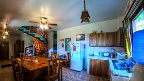 Una cocina con comedor, armarios de madera, un refrigerador, un lavamanos y una escalera espiral de colores.