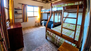 Una habitación rústica con literas de madera, una mesita pequeña y una ventana con cortinas.