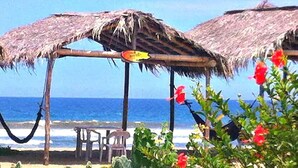 Escena de playa con sombrillas de paja, una hamaca y una mesa con sillas.