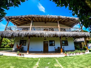 A two-story building with a thatched roof, wooden balconies, and a garden area with potted plants. - Casa Esperanto (Salango)