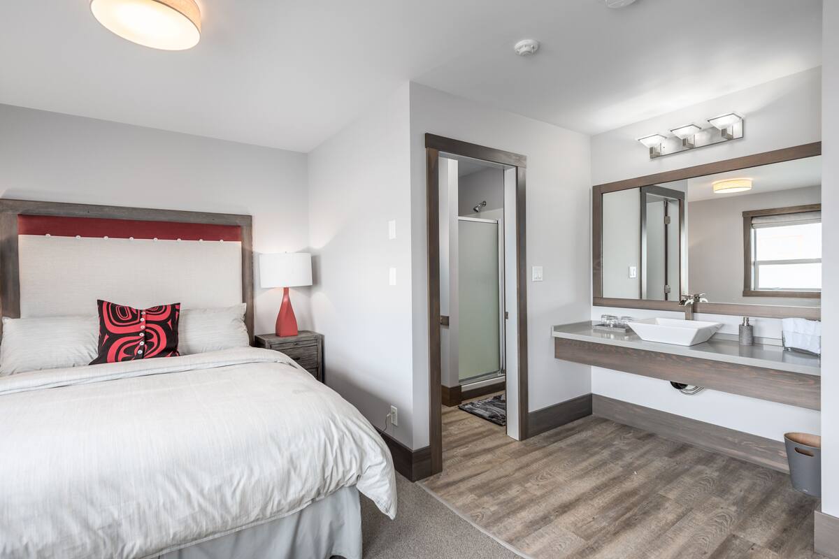 Ein modernes Hotelzimmer mit einem großen Bett, einem Badezimmer mit Waschtisch und einem begehbaren Kleiderschrank.