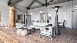 Een ruim buitgedeelte met een houten terras, witte meubels en een grote boomstam.