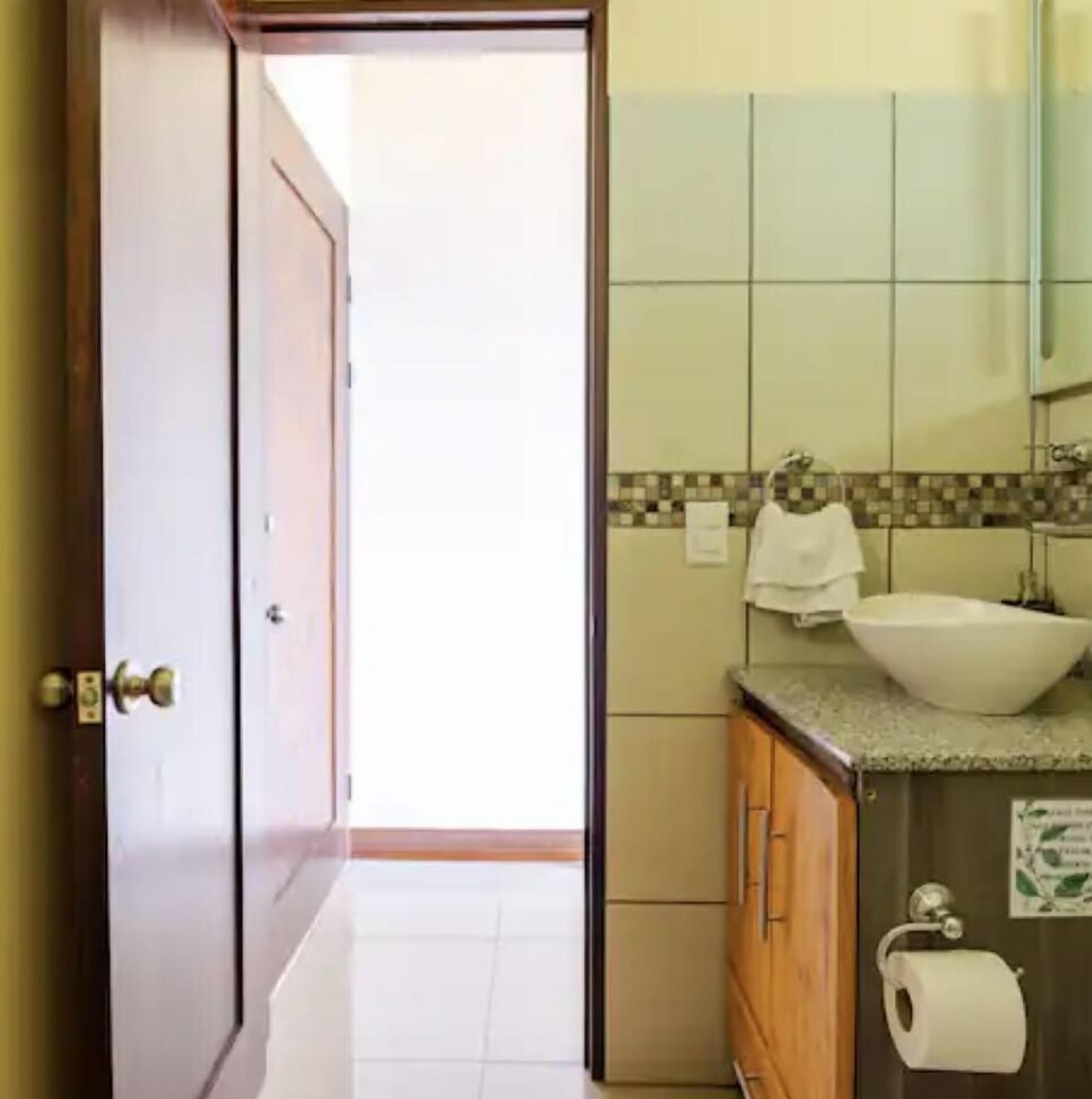 A bathroom with a white sink, a mirror, and a toilet paper holder.