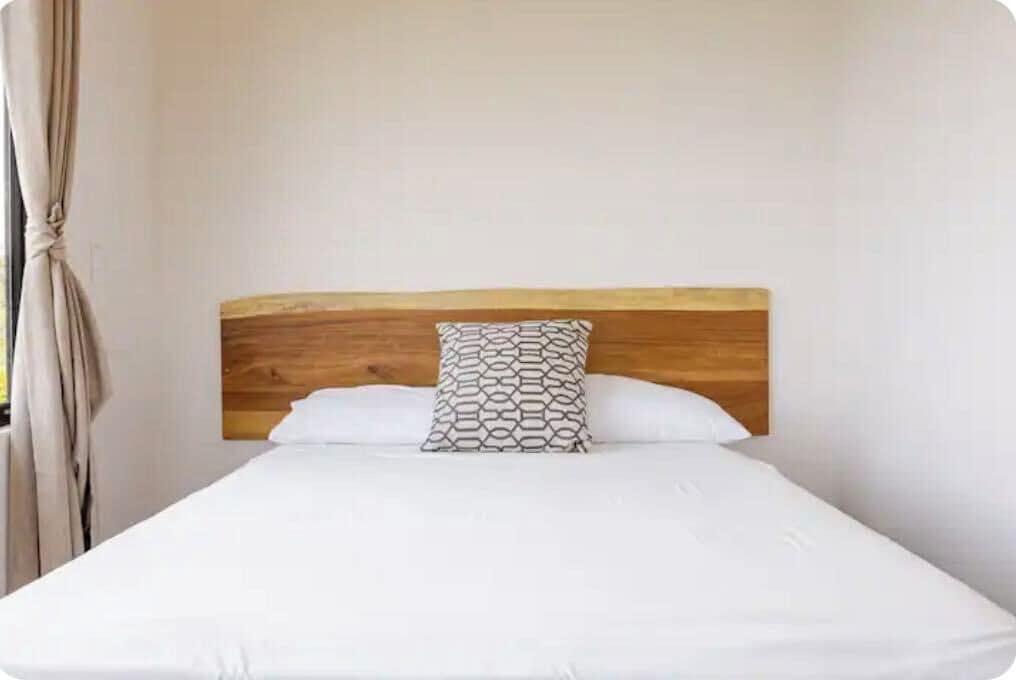 Una cama individual con cabecera de madera y un cojín estampado en una habitación con paredes blancas.