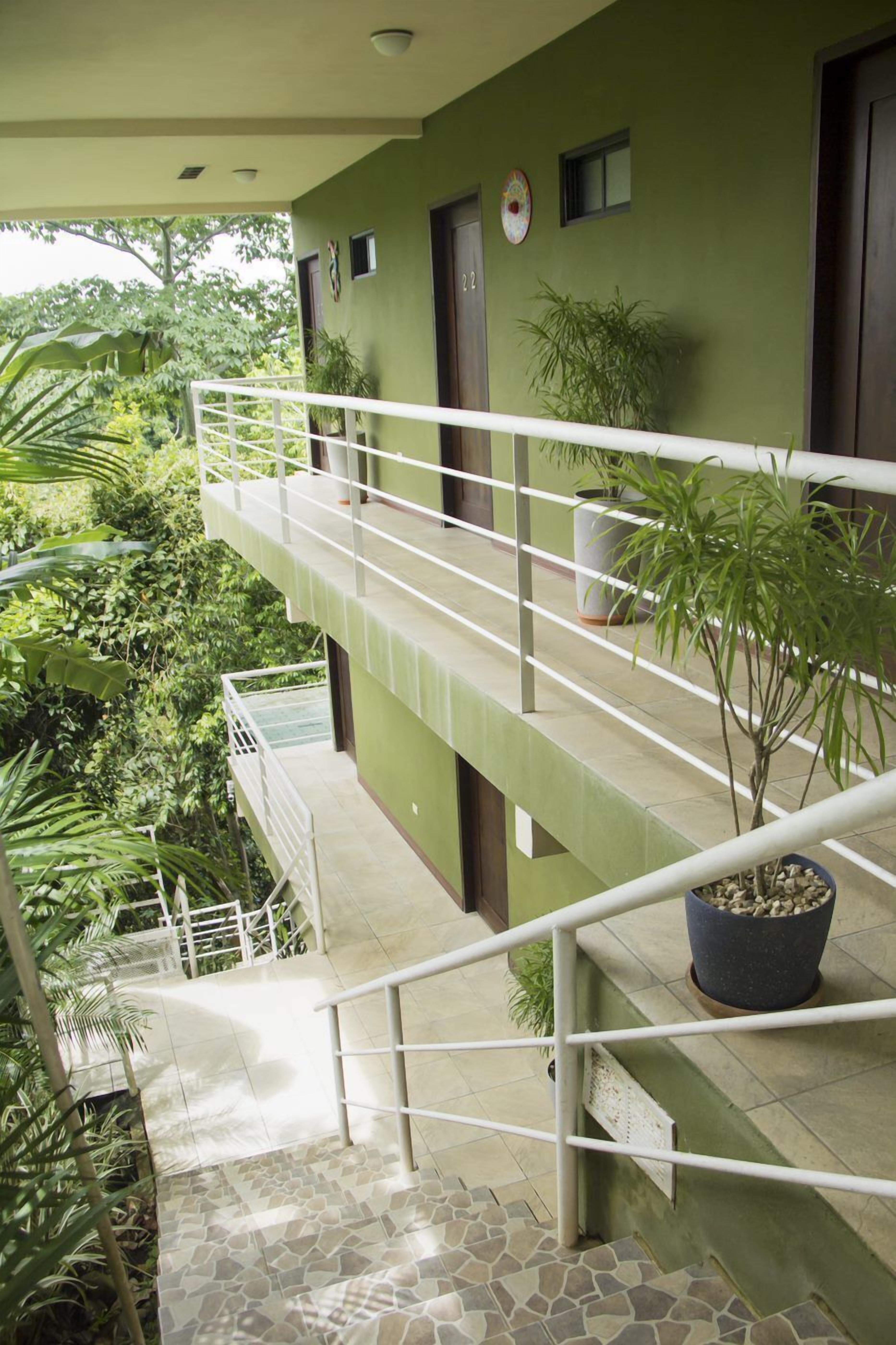 A multi-level building with a green exterior, a staircase with white railings, and potted plants.